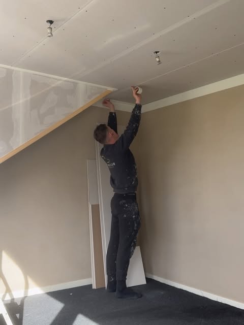 Gerrit werkt een plafondrand af in een kamer met warme beige muren